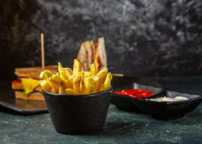 front-view-tasty-ham-sandwiches-with-french-fries-getting-eat-by-female-dark-surface